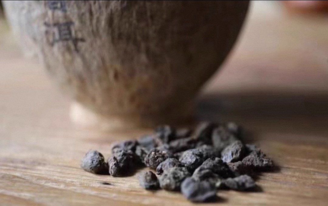 Alte Cha Tou Teeknollen auf einer Holztischfläche, dahinter eine beschriftete Kokosnussschale mit dem Schriftzug „普洱" – Symbolbild für gereiften Pu-Erh Tee aus Yunnan