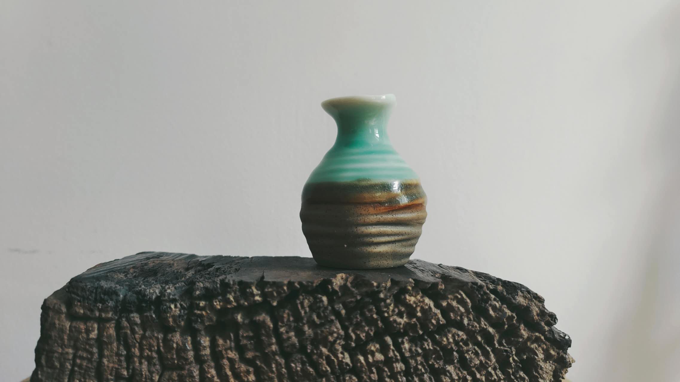 Unregelmäßig glasierte Keramikvase auf einem schlichten Holzpodest, Wabi-Sabi-Stillleben